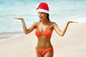 mujer vestida con bikini y gorro de navidad en la playa. vacaciones de invierno en los países cálidos. foto