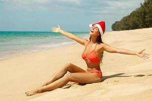 mujer vestida con bikini y gorro de navidad en la playa. vacaciones de invierno en los países cálidos. foto