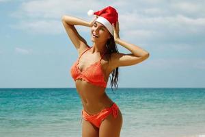mujer vestida con bikini y gorro de navidad en la playa. vacaciones de invierno en los países cálidos. foto