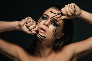 mujer con manchas de maquillaje en la cara y cepillos de rímel rotos foto