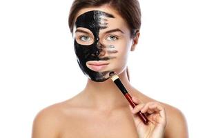 Beautiful woman is applying purifying black mask on her face photo
