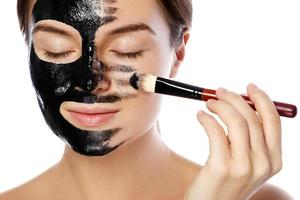 Beautiful woman is applying purifying black mask on her face photo