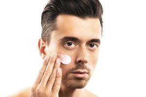 Young man is applying moisturizing cream on his face photo