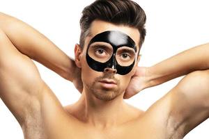 Young guy with a black charcoal mask on his face on white background. photo