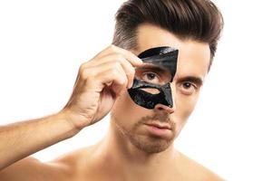 Young guy with a black charcoal mask on his face on white background. photo