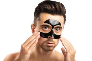 Young guy with a black charcoal mask on his face on white background. photo