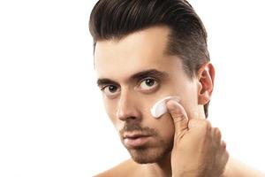Young man is applying moisturizing cream on his face photo