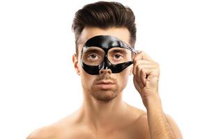 Young guy with a black charcoal mask on his face on white background. photo