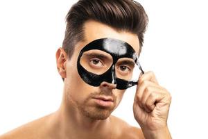 Young guy with a black charcoal mask on his face on white background. photo