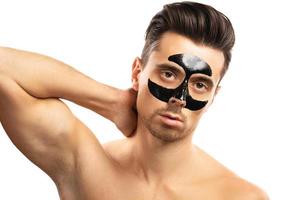 Young guy with a black charcoal mask on his face on white background. photo