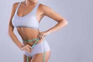 Woman is measuring her waistline against gray background photo