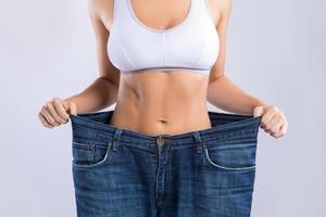 mujer feliz usando jeans después de la pérdida de peso sobre fondo gris foto