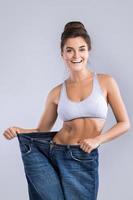 Happy woman wearing jeans after weight-loss on gray background photo