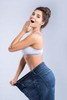 Happy woman wearing jeans after weight-loss on gray background photo