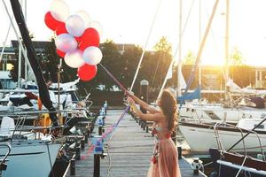 Woman in beautiful dress with a lot of colorful balloons on the yacht pier photo