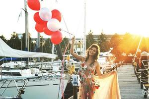 Woman in beautiful dress with a lot of colorful balloons on the yacht pier photo