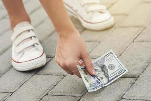 una mujer afortunada está recogiendo un billete de cien dólares del suelo. foto