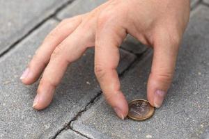mano femenina recogiendo una moneda de euro del suelo foto
