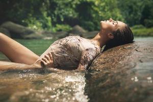 Sexy woman wearing shiny swimsuit is relaxing on the rocky beach photo