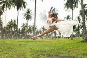 Beautiful bride is jumping in dance on the field with a lot of palm trees photo