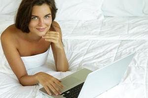 Woman lying on the bed and using laptop pc photo