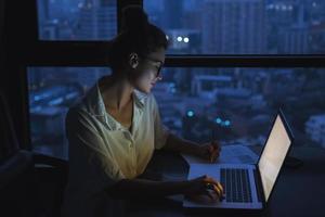 Woman is working with laptop at home during night. photo