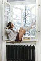 Woman is sitting on the windowsill and drinking hot tea or coffee photo