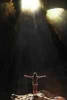 Hiker standing into the cave. Light rays come inside through holes into the rock. photo