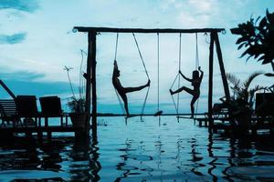 Silhouette of couple on swings which is above the water photo