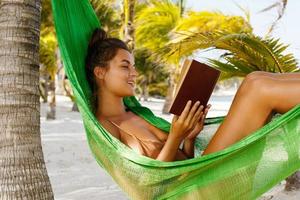 Happy and beautiful woman lying in the hammock and reading book photo