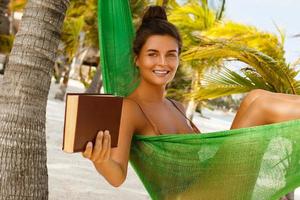 Happy and beautiful woman lying in the hammock and reading book photo