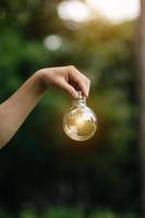 Hand holding light bulb on grass with solar energy and green background. power eco concept photo