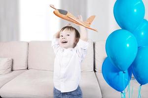 A handsome boy with joyful emotions on his face plays with toys and launches an airplane and a set of blue balloons. Happy Birthday. photo