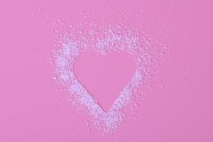 Top view of heart made of white sugar on pink background photo