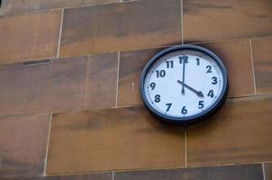 reloj redondo con número árabe adjunto en la pared de ladrillo de arena roja. foto