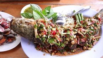 tailandese cibo, fritte testa di serpente pesce con erba salsa, citronella, kaffir lime le foglie su un' bianca piatto. video