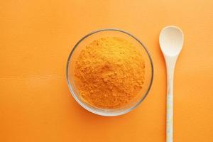 top view of turmeric root powder in bowl on orange color background photo