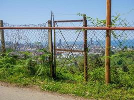 A beautiful city behind an old fence. Abandoned structure. Rusty metal. View from the mountain to the modern city. Beautiful cityscape. Batumi from above. photo
