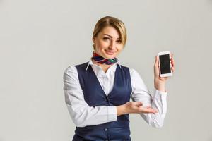 Hermosa joven azafata sosteniendo un teléfono inteligente aislado sobre fondo blanco. foto