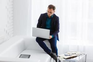 Doubtful young man looking up while working on laptop at home photo