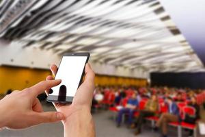 Man use mobile phone, blur image of people live in large conference room as background. photo