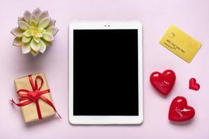 tableta digital para elegir regalos, hacer compras, sobres, corazones rojos en la vista superior de la mesa rosa lista de compras navideñas planas, feliz día de san valentín, fiesta, concepto de tienda en línea maqueta foto