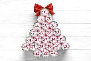 Advent calendar in shape of Christmas tree with numbers and ribbon instead of star on white wooden table Xmas advent calendar concept Top view Flat lay Holiday card photo