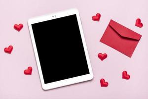 digital tablet for chooses gifts, makes purchase, envelope, red hearts on pink table Top view Flat lay Holiday shopping list, Happy Valentine's day, party, online shop concept Mock up photo