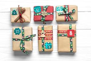 cajas de regalo rojas y verdes envueltas a mano decoradas con cintas, copos de nieve y números, adornos navideños y decoración en mesa blanca concepto de calendario de adviento de navidad vista superior tarjeta de vacaciones plana foto