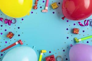 Colorful party frame with red gift box with various party confetti, balloons, streamers, pokers and decorations on blue background. Holiday card Flat lay Top view Happy Birthday party concept photo