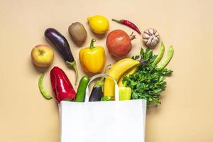 bolsa de papel ecológica con vegetales verdes orgánicos crudos aislados en fondo beige plano, vista superior cero desperdicio, concepto libre de plástico dieta saludable y desintoxicación, concepto de agricultura foto