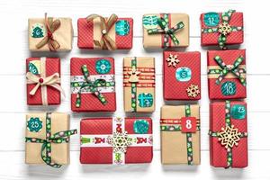 cajas de regalo rojas y verdes envueltas a mano decoradas con cintas, copos de nieve y números, adornos navideños y decoración en mesa blanca concepto de calendario de adviento de navidad vista superior tarjeta de vacaciones plana foto