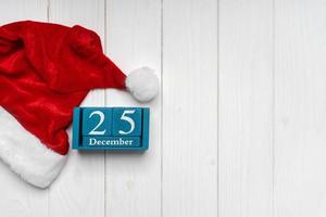 sombrero rojo de santa claus y calendario perpetuo azul sobre fondo blanco de madera foto