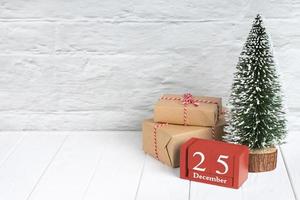 Decorative christmas tree, gift boxes and wooden calendar on white wooden background. photo